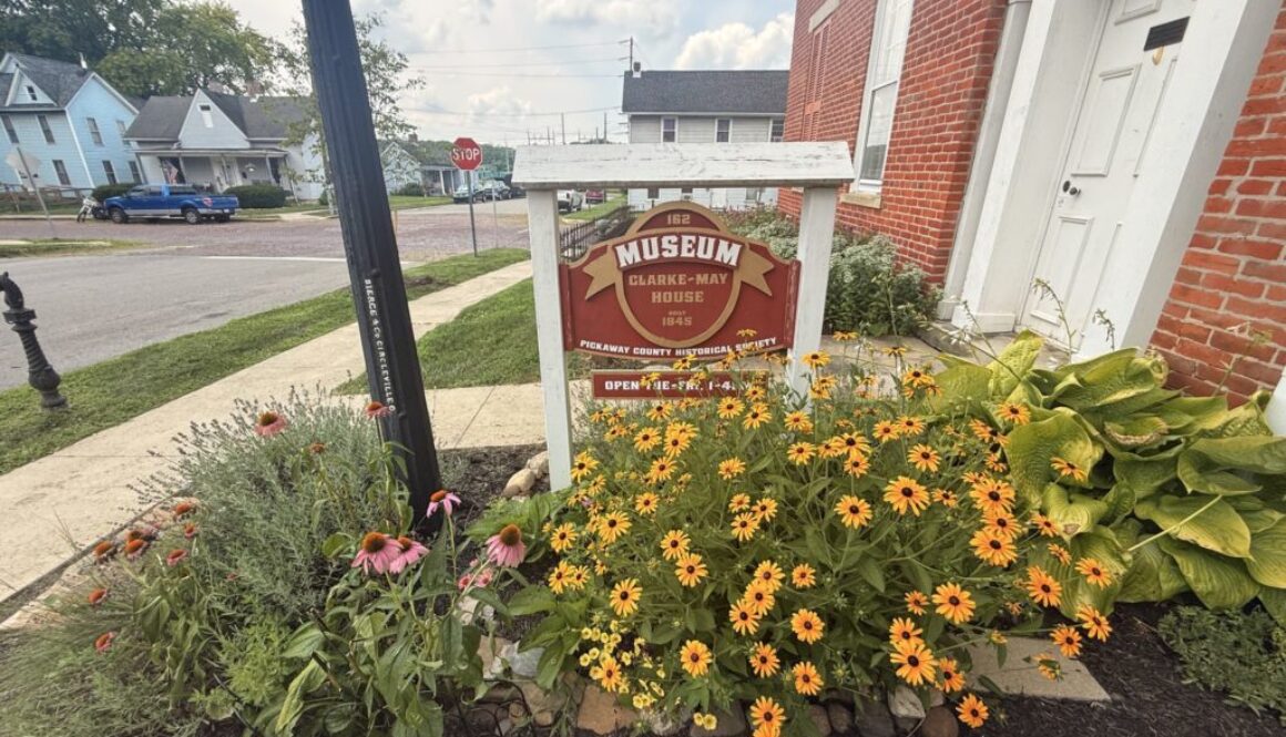 Exterior of Clarke-May Museum in Circleville, Ohio, with historic building, garden flowers, and museum sign in front.