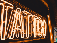Image of orange neon sign saying "Tattoo" and the stained pumpkin tattoo convention logo in the corner.