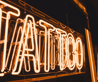 Image of orange neon sign saying "Tattoo" and the stained pumpkin tattoo convention logo in the corner.
